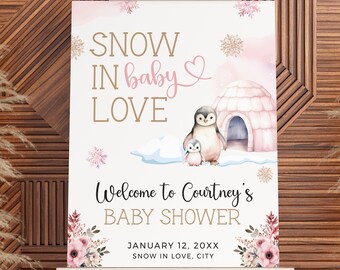 May include: A pink and white welcome sign for a baby shower with the text "SNOW IN baby LOVE" and a penguin family. The sign also includes the text "Welcome to Courtney's BABY SHOWER", "JANUARY 12, 20XX", and "SNOW IN LOVE, CITY".