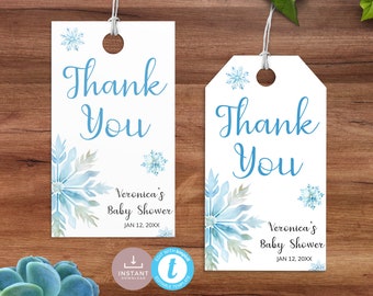 以下が含まれることがあります： 水色の筆記体で「Thank You」と書かれた2つの白いギフトタグ。タグには、青とグレーの色合いの雪の結晶と花のウォーターカラーデザインが施されています。「Veronica's Baby Shower, Jan 12, 20XX」というテキストも印刷されています。