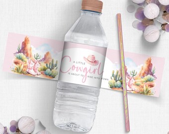 May include: Water bottle label with a pink background and a watercolor illustration of a desert landscape. The text on the label reads "A little cowgirl is about to ride into town".