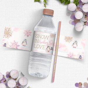 May include: Water bottle label with a pink and gold design featuring penguins and snowflakes. The text on the label reads "Snow in Baby Love" and "Courtney's Baby Shower 12.12".
