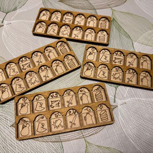 May include: Four wooden game trays, each with laser-cut game pieces. The pieces feature swords, barrels, and flags. The trays are arranged on a patterned surface. The game pieces are made of wood.