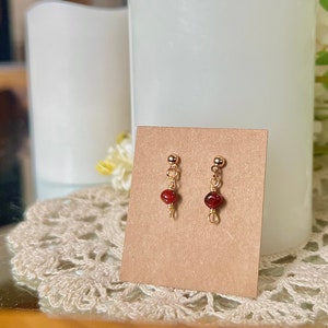 May include: A pair of gold stud earrings with a single red gemstone on each earring.
