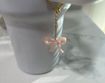 May include: A delicate gold chain with a pink bow charm. The bow has a small rhinestone in the center.