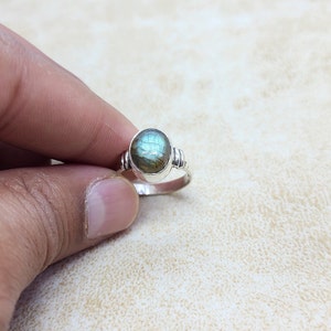 May include: A silver ring with a round, iridescent green labradorite gemstone. The ring has a simple band with a textured detail on either side of the stone.