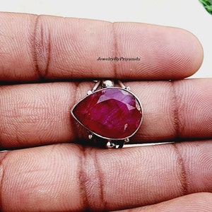 May include: A sterling silver ring with a large, teardrop-shaped ruby gemstone. The ring is set with small silver accents around the gemstone.