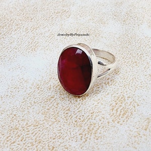 Puede incluir: Un anillo de plata con una gran piedra preciosa roja oscura de forma ovalada. El anillo tiene un diseño simple y elegante.