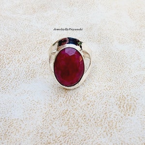 May include: A silver ring featuring a large, oval-shaped, deep red gemstone set in the centre. The ring has a simple, elegant design.