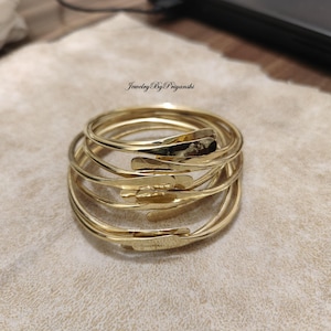 May include: A set of six gold-toned metal bangles stacked on top of each other. The bangles are smooth and have a slightly hammered texture.