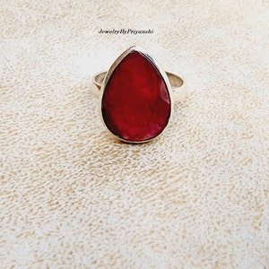 Peut inclure: Une bague en argent avec une pierre de rubis en forme de larme. Le rubis est de couleur rouge foncé et est entouré d'une bande d'argent.