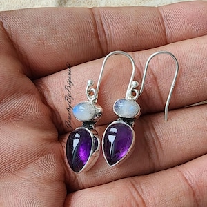 May include: A pair of silver dangle earrings with a teardrop-shaped amethyst gemstone and a round moonstone gemstone.