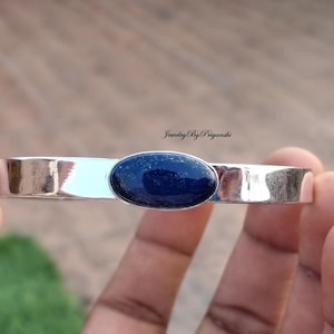May include: A silver bangle bracelet with a dark blue oval lapis lazuli gemstone set in the center.