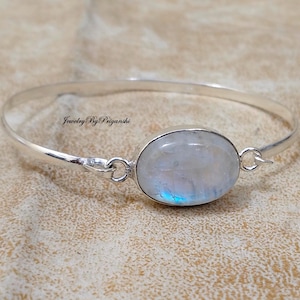 Op de afbeelding: Een zilveren armband met een grote ovale maansteen. De steen heeft een melkachtig witte kleur met een blauwe iriserende glans.