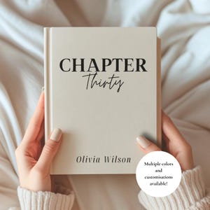 May include: A cream-colored hardcover book featuring the black printed text CHAPTER Thirty at the top and the name Olivia Wilson at the bottom. The book has a smooth, matte finish and is held upright, displaying a clean, minimalist front cover design.