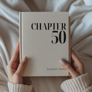 May include: A hardcover book with the words "CHAPTER 50" in black font. The name "Jennifer Smith" is printed below. The book is held by a person wearing a cream-colored sweater.