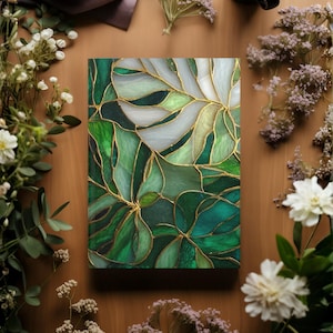 May include: A journal with a stained glass design featuring green and white leaves with gold accents. The cover is surrounded by white and purple flowers on a wooden surface.