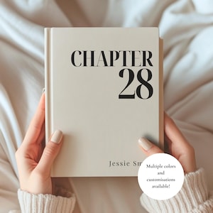 Puede incluir: Un libro de tapa dura de color crema con el texto negro CHAPTER 28 mostrado de forma prominente en la portada, con el nombre Jessie Sm impreso en una fuente más pequeña en la parte inferior. El libro se sostiene frente a un fondo neutro.