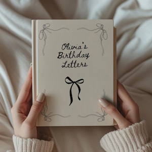 May include: A cream-coloured book titled "Olivia's Birthday Letters" with black script and bow illustrations. The book is held by a person wearing a cream-coloured jumper. The cover features a large bow and smaller bow designs.