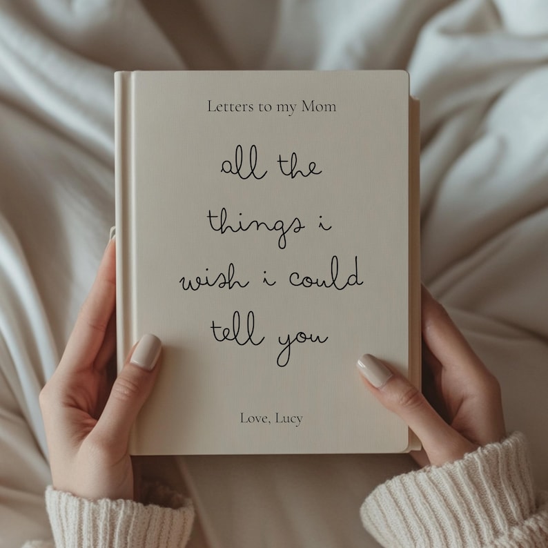 Może przedstawiać: Kremowa książka zatytułowana "Letters to my Mom" trzymana otwarta. Okładka zawiera odręczny tekst: "all the things i wish i could tell you." Poniżej znajduje się "Love, Lucy."