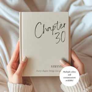 Puede incluir: Un libro de tapa dura de color crema con el texto Chapter 30 en letra cursiva negra, el nombre SAMANTHA en letras mayúsculas negras y el texto Every chapter brings new growth en fuente negra. Un gráfico circular blanco contiene el texto Multiple colors and customisations available!