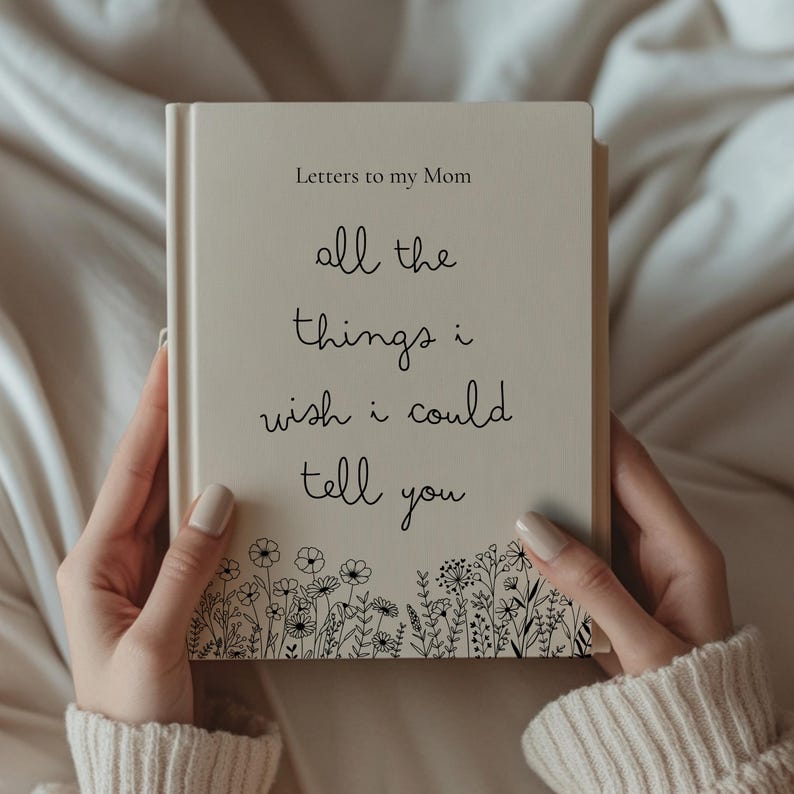 May include: A cream-colored journal titled "Letters to my Mom" with the inscription "all the things i wish i could tell you." The cover features a floral border design. The journal is held by a person.