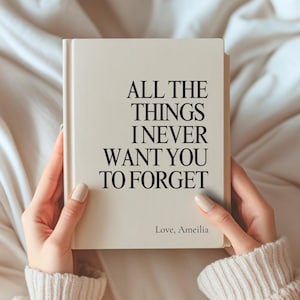 May include: A cream-coloured hardcover book with black text on the front cover that reads ALL THE THINGS I NEVER WANT YOU TO FORGET and Love, Ameilia at the bottom. The book has a clean, matte finish and a simple, bold sans-serif typeface.