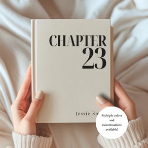 May include: A cream-coloured hardback book featuring the black text "CHAPTER 23" prominently displayed on the front cover, with the name "Jessie Sm" printed in a smaller font near the bottom. The book has a clean, smooth finish and a spine.