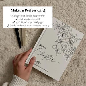 May include: A white notebook with a floral design and the words "The next Chapter" in script. The notebook is 5.75" x 8" with 150 lined pages and a sturdy hardcover matte laminate coating. A black pen and a beige lipstick are next to the notebook.
