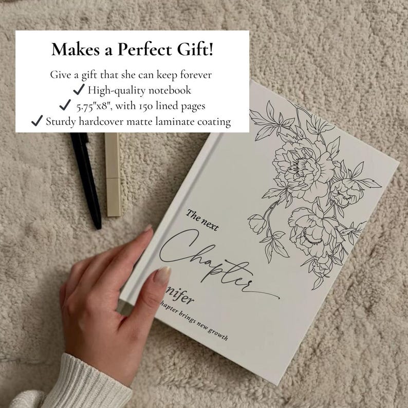 May include: A white notebook with a floral design and the words "The next Chapter" in script. The notebook is 5.75" x 8" with 150 lined pages and a sturdy hardcover matte laminate coating. A black pen and a beige lipstick are next to the notebook.