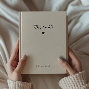 May include: A cream-colored book with the words "Chapter 40" and a heart symbol printed in black. The name "Julianne Smith" is printed below. The book is held by a person wearing a cream-colored sweater.