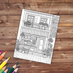May include: A black and white line drawing of a storefront with a balcony, awning, and shelves filled with produce. The storefront is a two-story building with a door and windows. There are plants and flowers in pots outside the building.