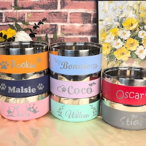 Może przedstawiać: Sześć misek ze stali nierdzewnej dla zwierząt domowych z personalizowanymi nazwami, w tym Rookie, Maisie, Bonnie, Coco, Oscar i Willow. Miski są ułożone parami i mają różne kolorowe paski z wygrawerowanymi nazwami i odciskami łap.