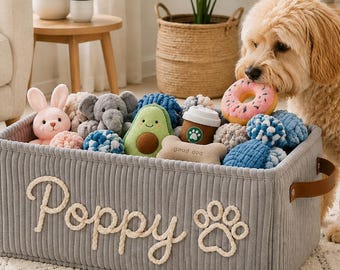 May include: A rectangular grey corduroy storage basket with brown leather handles, featuring the name Poppy and a paw print embroidered in white rope. The basket is filled with various plush dog toys, including an avocado, donut, and bone.