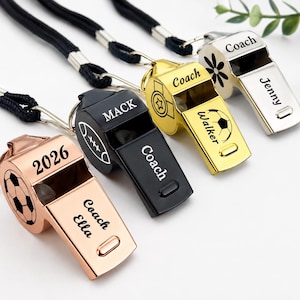 Pode incluir: Quatro apitos de metal com acabamentos em ouro rosa, preto, dourado e prateado, cada um preso a um cordão preto. Os apitos apresentam gravações personalizadas com nomes como Ella, Mack, Walker e Jenny, além de ícones esportivos e o ano 2026.
