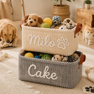 Peut inclure: Deux paniers de rangement rectangulaires en velours c&ocirc;tel&eacute; empil&eacute;s verticalement. Le panier sup&eacute;rieur est cr&egrave;me avec le nom Milo et une empreinte de patte brod&eacute;s en blanc. Le panier inf&eacute;rieur est gris avec le nom Cake brod&eacute; en blanc. Poign&eacute;es marron.
