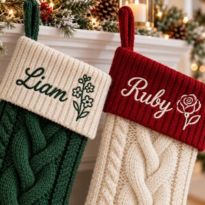 May include: Two cable-knit Christmas stockings with hanging loops. The left stocking is dark green with a cream cuff embroidered with the name Liam and a flower. The right stocking is cream with a red cuff embroidered with the name Ruby and a rose.