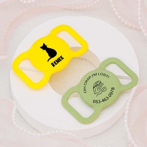 May include: Two yellow and green plastic dog collar tags. The yellow tag has a black silhouette of a cat and the text "Renee". The green tag has a wave graphic and the text "Oh crap! I'm lost! 053-463-0978".
