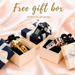 May include: Three metal whistles with black lanyards, each featuring custom engravings of names, titles like Coach, and football graphics. The whistles are presented in small square gift boxes with lids and ribbons, displayed on a soft fabric.