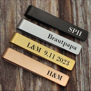 Może przedstawiać: Cztery spinki do krawata w różnych kolorach: czarny, srebrny, złoty i różowe złoto. Każda spinka do krawata ma inny grawerowany napis: "SPH", "Brautpapa", "L&M 9.11 2023" i "H&M".