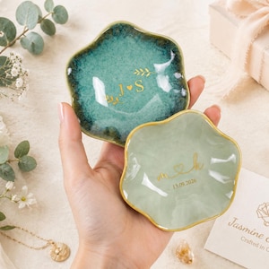 May include: Two small, scalloped-edge ceramic trinket dishes with gold-painted rims. The larger dish is a deep teal with a glossy finish, featuring the gold text J heart S. The smaller dish is a pale sage green with the gold text m heart k and 13.09.2026.