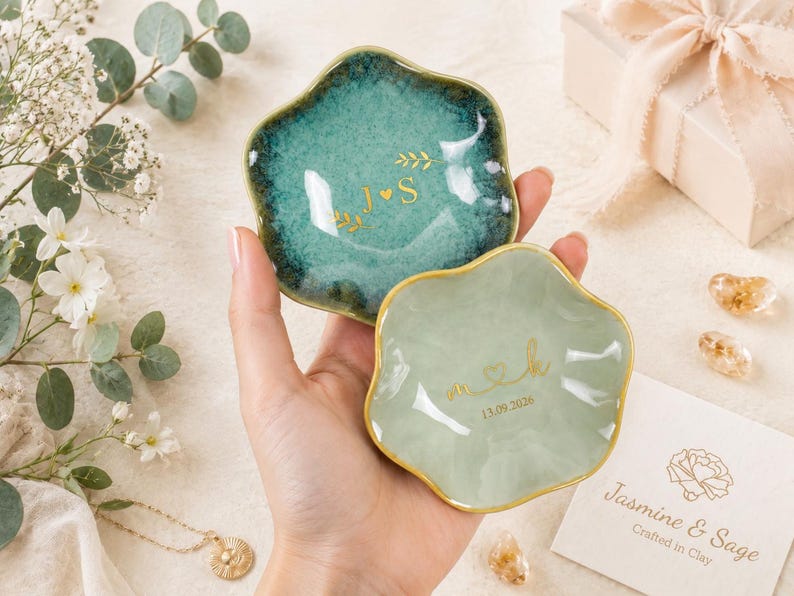 May include: Two small, scalloped-edge ceramic trinket dishes with gold-painted rims. The larger dish is a deep teal with a glossy finish, featuring the gold text J heart S. The smaller dish is a pale sage green with the gold text m heart k and 13.09.2026.