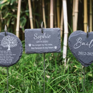 May include: Three dark grey slate pet memorial garden stakes. One is round with a tree design and the name "Chole". Another is rectangular with the name "Sophie". The third is heart-shaped with the name "Bailey". All have dates.