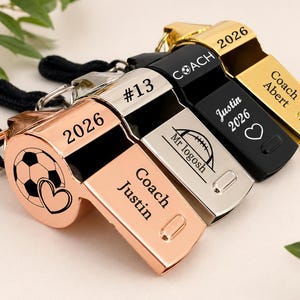 May include: Four metal whistles in rose gold, silver, black, and gold finishes, each attached to a black lanyard. The whistles feature custom engravings including the text Coach Justin, 2026, #13, Mr logosh, Coach Abert, and various sports icons.