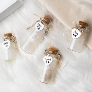 May include: Four small glass bottles with cork stoppers, each containing a white substance. Each bottle has a heart-shaped tag with a pet's name: Olive, Thor, Zeus, and Peanut. The tags have paw prints, a bone, and a crown.