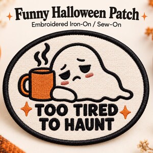 May include: An oval embroidered iron-on or sew-on patch with a cream background and black border. It features a white ghost with pink cheeks leaning on an orange mug with steam, and the black text "TOO TIRED TO HAUNT" with two orange stars.