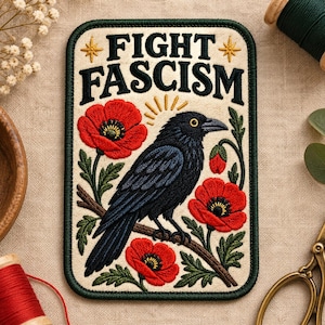 Può includere: Una toppa ricamata rettangolare con sfondo color crema e bordo verde scuro. Raffigura un corvo nero appollaiato su un ramo marrone circondato da papaveri rossi e foglie verdi. Il testo FIGHT FASCISM è ricamato in nero.