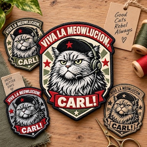 May include: Four embroidered patches featuring a cat wearing a black beret with a red star and a headset. The text reads VIVA LA MEOWLUCION and CARL!. The patches are in various color schemes including red, green, black, and cream, displayed on a wooden surface.