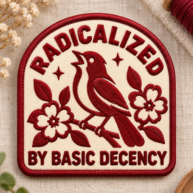 May include: An embroidered patch with a cream background and dark red border. It features a dark red bird perched on a branch with flowers. The text RADICALIZED is arched above the bird, and BY BASIC DECENCY is printed at the bottom in red.
