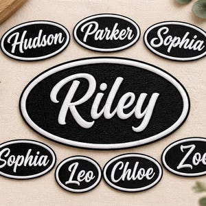 Puede incluir: Una colección de parches ovalados negros con bordes blancos y nombres bordados en blanco que incluyen Hudson, Parker, Sophia, Riley, Leo, Chloe y Zoe. Los parches presentan una fuente en relieve estilo cursiva para cada nombre.