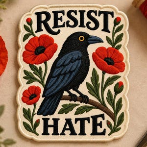 Könnte beinhalten: Ein rechteckiger, bestickter Aufnäher mit gewelltem Rand, der eine schwarze Krähe auf einem Ast zeigt, umgeben von roten Mohnblumen und grünen Blättern. Der Text RESIST ist oben und HATE unten in Schwarz auf cremefarbenem Grund gestickt.