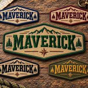 May include: Five hexagonal embroidered patches featuring the word MAVERICK in bold lettering. Each patch displays a mountain range, pine trees, and a compass star. The patches come in various colour combinations including blue, red, green, and gold.